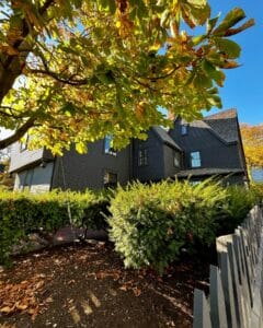 Bright autumn leaves and lush green shrubs create a natural frame for the House of the Seven Gables in Salem, Massachusetts, highlighting its dark wooden exterior.
