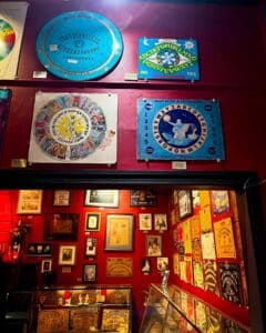 A colorful wall at the Salem Witch Board Museum featuring unique Ouija board designs, including circular and astrological-themed boards, alongside vintage advertisements and historical artifacts.