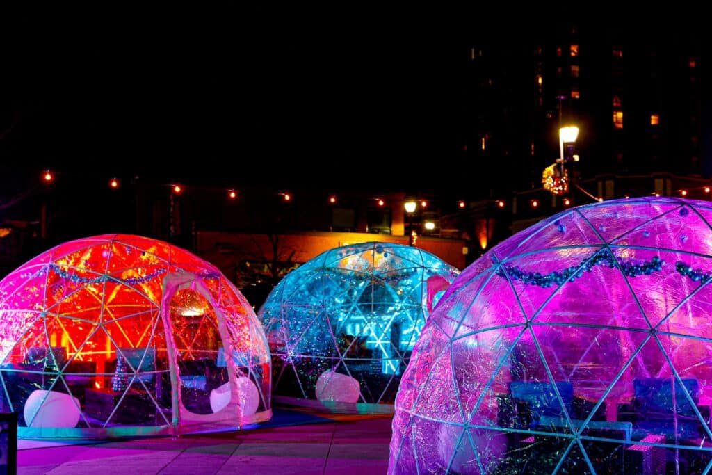 A row of transparent igloos illuminated with colorful lights in red, blue, and purple during a nighttime event in Salem, Massachusetts.