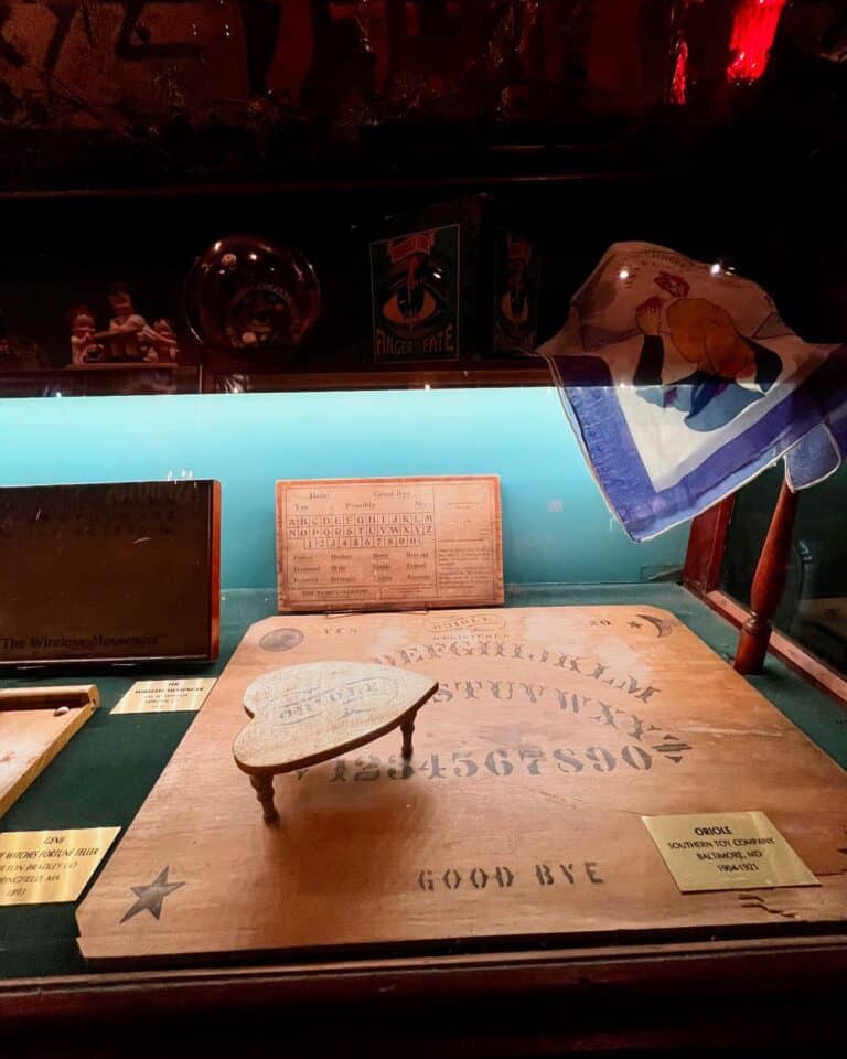 A display case at the Salem Witch Board Museum in Salem, Massachusetts, showcasing a vintage Ouija board, planchette, and historical spirit communication artifacts.