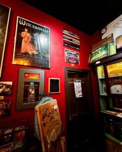 A red-walled exhibit at the Salem Witch Board Museum featuring vintage witch board posters, collectible board games, and mysterious artifacts.