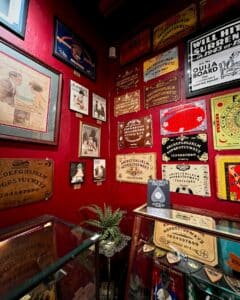 A vibrant wall display at the Salem Witch Board Museum in Salem, Massachusetts, featuring a diverse collection of vintage Ouija boards in various colors and styles, framed art, and historical advertisements.