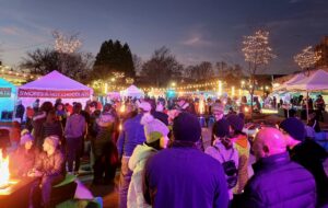 Visitors in Salem Massachusetts enjoying a winter evening at the Frozen Fire Festival, gathering around small fire pits, savoring s’mores and hot chocolate, and browsing under soft glowing lights.