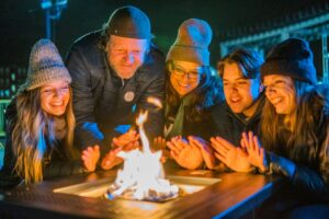 A group of friends and family in Salem Massachusetts gathered around a fire pit, enjoying warmth and laughter at the Frozen Fire Festival.