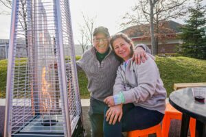 A smiling couple sits near a patio heater at the Salem Frozen Fire Festival, enjoying the festive outdoor setting in Salem, Massachusetts.