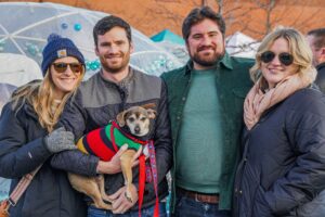 A group of friends in Salem Massachusetts posing with a small dog in a festive sweater, enjoying the Frozen Fire Festival.