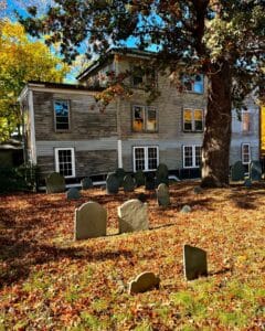 A serene autumn scene at Old Burying Point Cemetery in Salem Massachusetts, showcasing historic headstones surrounded by fallen leaves and vibrant fall foliage.