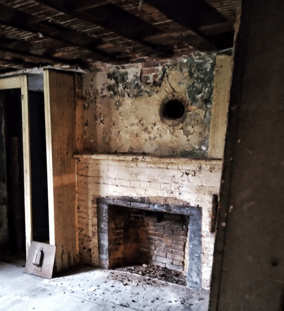 This image shows the interior of the Gedney House in Salem, Massachusetts, highlighting an aged and partially deteriorated brick fireplace. The weathered plaster walls, exposed brickwork, and unfinished wooden ceiling beams reflect the house’s long history and centuries of use. This fireplace, likely a central feature in the home's early colonial life, would have served both practical and social purposes, providing warmth and a space for cooking. The preservation of this historic interior offers visitors a raw and authentic glimpse into 17th-century architecture and everyday life in early New England.