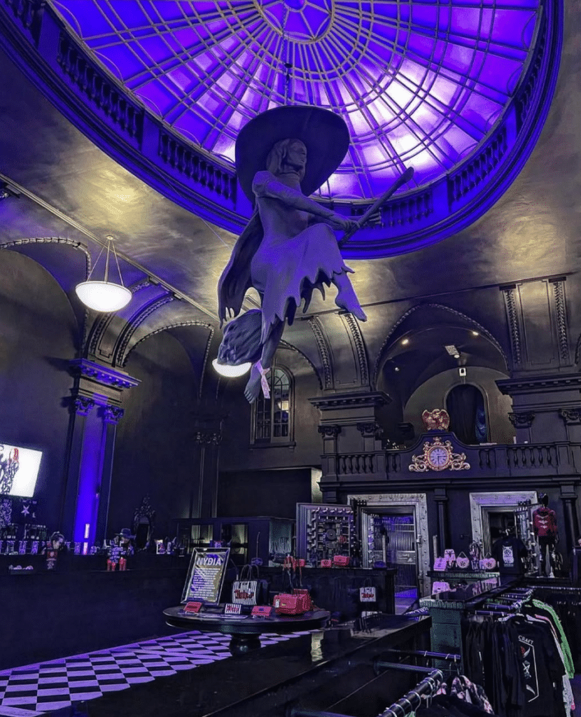 The illuminated interior of Blackcraft Salem in Salem, Massachusetts, featuring a witch sculpture flying on a broom under a glowing purple dome, surrounded by gothic decor and merchandise displays.