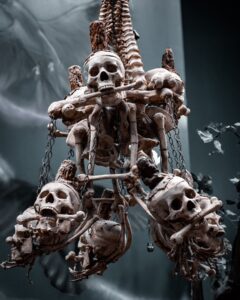 A haunting chandelier made of human skulls and bones, displayed in Salem, Massachusetts, surrounded by eerie shadows and chains.