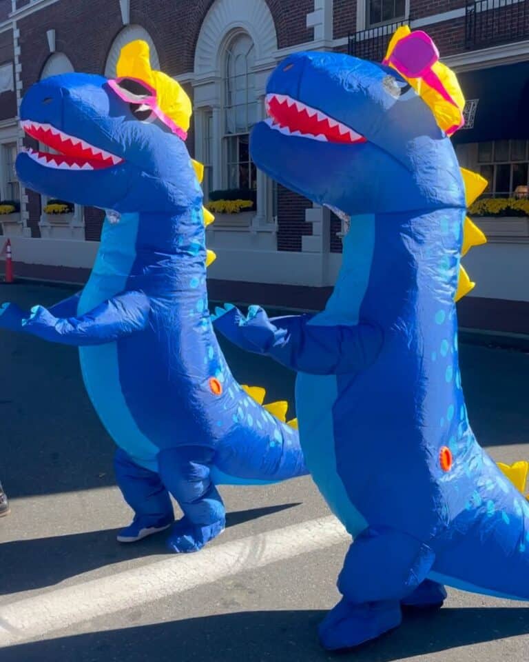 Two people dressed in inflatable blue dinosaur costumes with sunglasses and yellow hats stand outside the historic Hawthorne Hotel in Salem, Massachusetts.