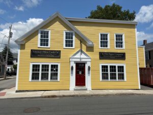 A sunny yellow building housing Ye Olde Pepper Companie in Salem, Massachusetts, labeled as America's oldest candy company, with a red door and charming black signs.