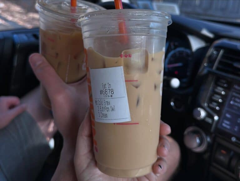 Two Dunkin’ iced coffees being held inside a car, one labeled with “Cold Brew, 3 Brown Sugar Swirl, 3 Cream,” capturing a casual moment in Salem, Massachusetts.