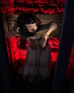 A haunting exhibit at the Salem Museum of Torture depicting a bound woman in stocks with bloodied injuries, illuminated by eerie red lighting against a stone wall backdrop, representing the torment of accused witches.
