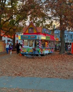 A vibrant cotton candy and snow cone stand at Salem Common in Salem Massachusetts, surrounded by autumn leaves and people enjoying the festive atmosphere.