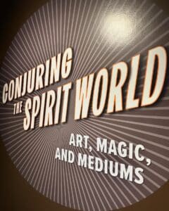 A sign reading "Conjuring the Spirit World: Art, Magic, and Mediums" displayed at the Peabody Essex Museum in Salem, Massachusetts. The design features bold, glowing text against a radiating background pattern.