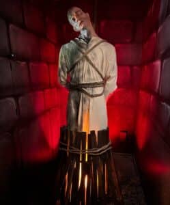 A mannequin tied to a wooden stake with simulated fire effects, illuminated in red lighting, at the Salem Museum of Torture in Salem, Massachusetts.
