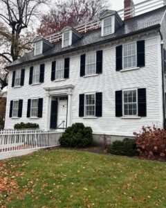 The historic Ropes Mansion in Salem, Massachusetts, a white colonial-style house with black shutters, a white picket fence, and a neatly kept yard adorned with autumn leaves.