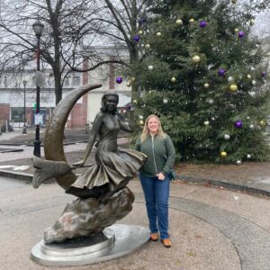 A person poses next to the Bewitched statue of Samantha Stephens in Salem, Massachusetts, with a decorated Christmas tree in the background.