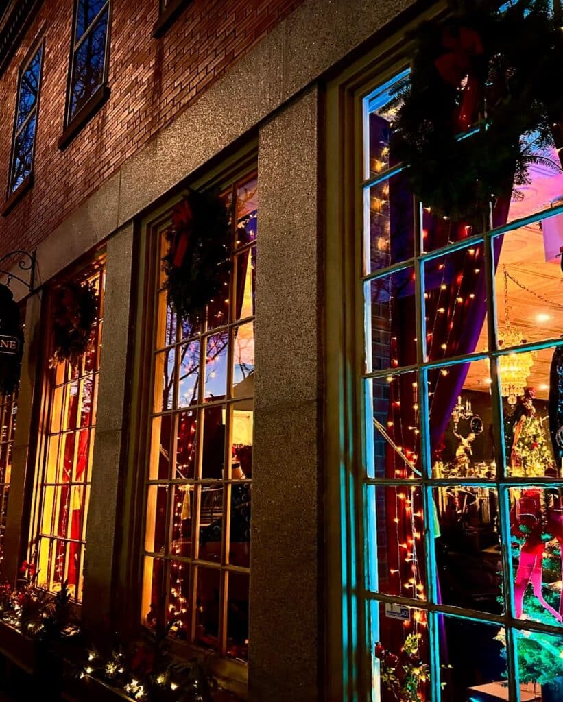 A warmly lit window in Salem, Massachusetts, decorated with holiday wreaths and twinkling lights, offering a peek into the festive interior.
