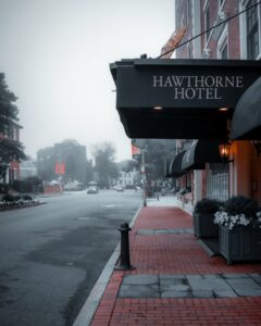 A misty view of the iconic Hawthorne Hotel's awning with a quiet red-brick sidewalk and blurred historic buildings in Salem, Massachusetts.