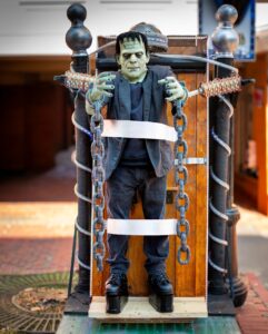A life-sized Frankenstein figure in chains, displayed on a wooden platform with electrifying props in downtown Salem, Massachusetts.