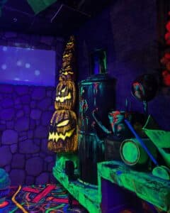 A glow-in-the-dark Halloween display in Salem, Massachusetts, featuring stacked jack-o'-lanterns and a spooky cauldron scene with vibrant colors and eerie lighting.