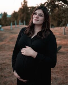 A serene image of a pregnant woman dressed in black, cradling her belly, with soft sunset lighting and a historic cemetery backdrop in Salem, Massachusetts.
