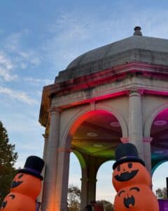 A festive Halloween display at Salem Common in Salem Massachusetts, featuring large inflatable jack-o'-lanterns in front of a historic stone pavilion with colorful lights illuminating the arches.