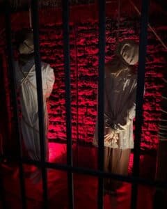 wo mannequin figures, bound and hooded, hanging in a dimly lit exhibit with red illumination at the Salem Museum of Torture in Salem, Massachusetts.