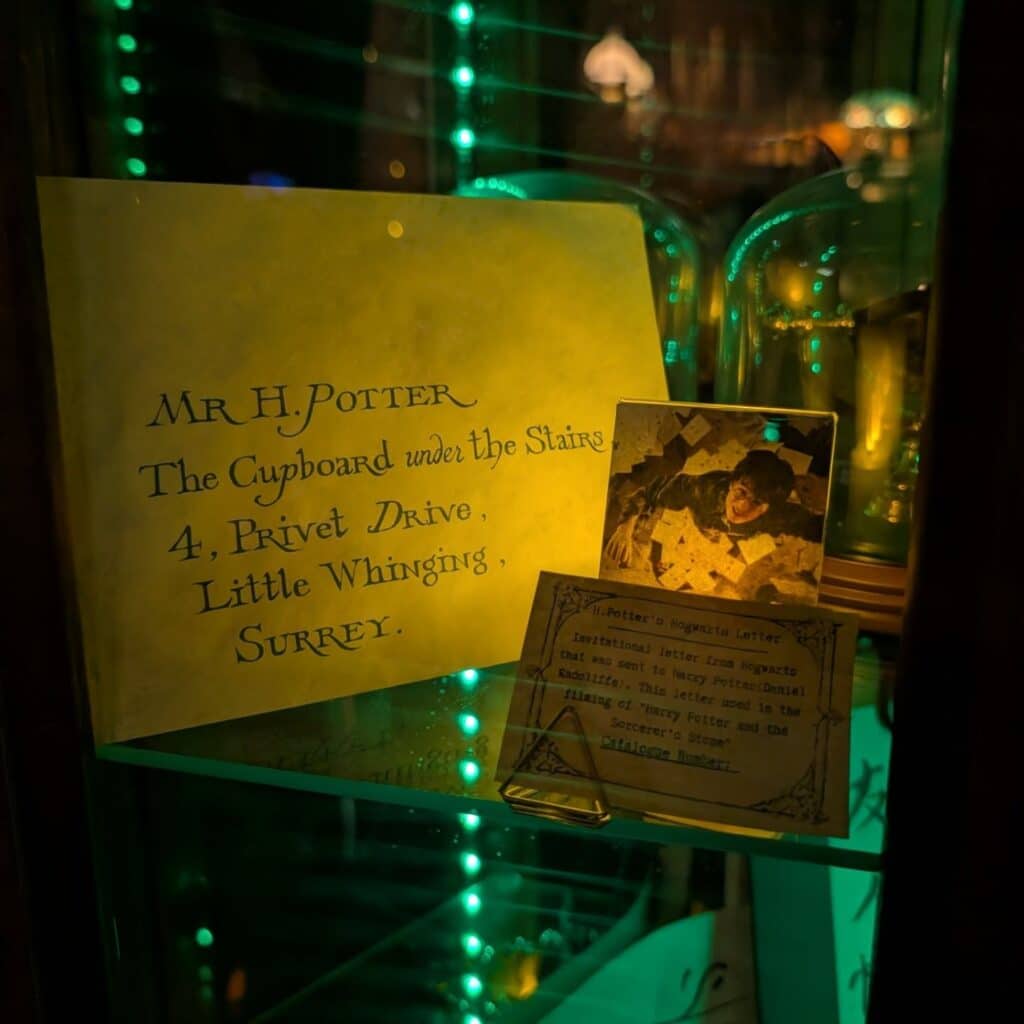 A display featuring Harry Potter’s acceptance letter addressed to "The Cupboard under the Stairs," along with a photo of the iconic scene and a description, illuminated by green lighting.