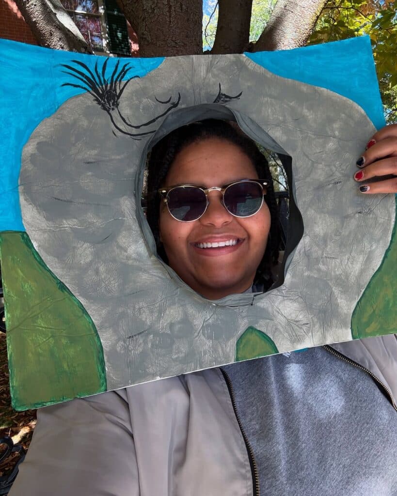 A cheerful person holding a fun handmade frame outdoors in Salem, Massachusetts, with colorful painted designs that make the scene playful and unique.