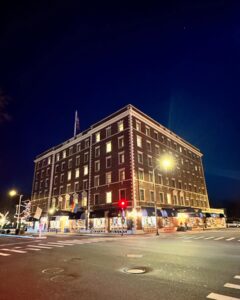 The historic Hawthorne Hotel in Salem, Massachusetts, illuminated at night with warm lights, standing prominently on a quiet corner with holiday decorations in the windows.