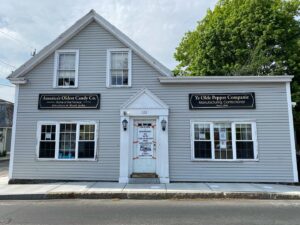 A gray historic building housing Ye Olde Pepper Companie in Salem, Massachusetts, with signs identifying it as America's oldest candy company and the home of famous Gibralters and Black Jacks.