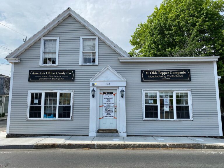 A gray historic building housing Ye Olde Pepper Companie in Salem, Massachusetts, with signs identifying it as America's oldest candy company and the home of famous Gibralters and Black Jacks.