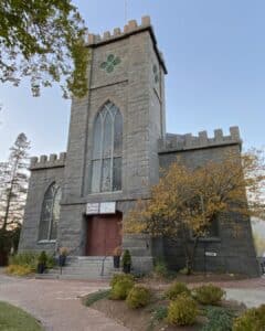 A view of the First Church of Salem in Massachusetts, a Gothic-style stone building with tall windows and crenellated rooflines, adorned with a Black Lives Matter banner.