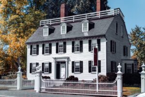 The Ropes Mansion in Salem, Massachusetts, a historic white house with black shutters, framed by colorful autumn trees and a white picket fence.
