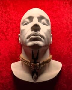 A detailed exhibit at the Museum of Torture in Salem, Massachusetts, featuring a lifelike head model displaying a medieval neck torture device against a striking red background.
