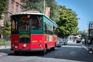 The red and green Hawthorne trolley parked on a sunny street in Salem, Massachusetts, surrounded by historic buildings and lush trees.