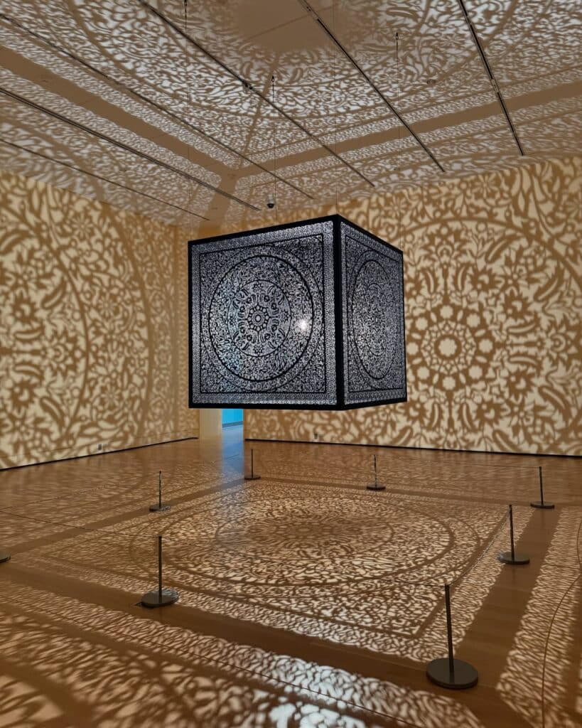 An intricate metal cube art installation at the Peabody Essex Museum in Salem Massachusetts casts beautiful patterns of light and shadow across the walls, ceiling, and floor of the gallery.