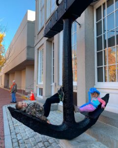 Two children playing on a large black anchor outside the Peabody Essex Museum in Salem, Massachusetts, enjoying a sunny autumn day.