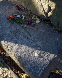 A stone memorial bench dedicated to Margaret Scott, one of the victims of the Salem Witch Trials, engraved with the date "Sept. 22, 1692." Flowers, coins, and small tokens are left as tributes at the Salem Witch Trials Memorial in Salem, Massachusetts.