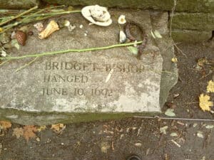 The memorial stone for Bridget Bishop, the first person hanged during the Salem Witch Trials, adorned with offerings like flowers, shells, and pinecones in Salem, Massachusetts.
