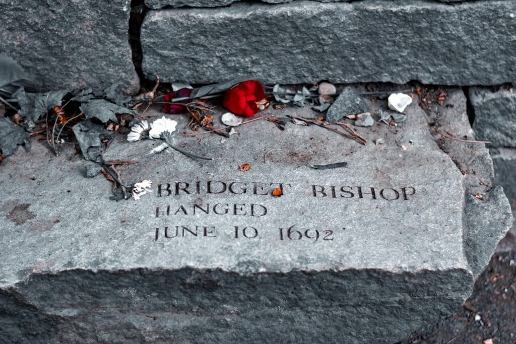 A close-up of Bridget Bishop's memorial stone at the Salem Witch Trials Memorial in Salem, Massachusetts, adorned with scattered flowers and leaves as a tribute to her memory.