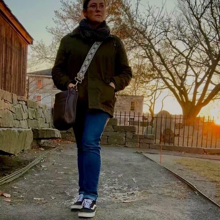 A person walking through the Salem Witch Trials Memorial in Salem, Massachusetts, surrounded by stone walls and a wooden structure, with the golden sunset creating a serene and reflective atmosphere.