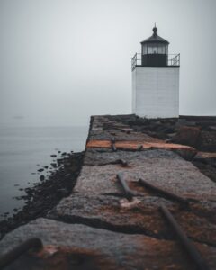 Derby Lighthouse in Salem, Massachusetts, seen at the end of a rugged stone pathway with rusted iron rods, surrounded by misty waters.