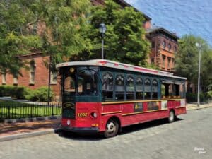 Red Salem Trolley on a sunny day in Salem, Massachusetts, with charming brick buildings and greenery in the background.