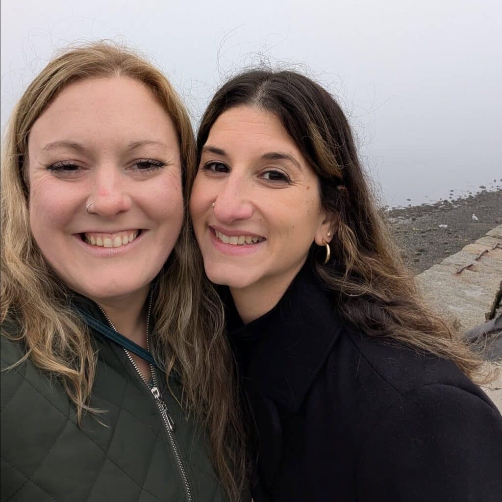 Two smiling friends pose for a selfie by the Salem waterfront on a foggy day, with the rocky shore and misty horizon in the background.