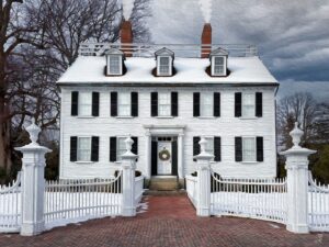 The Ropes Mansion in Salem, Massachusetts, covered in snow, with smoke rising from its chimneys and a festive wreath hanging on the front door, framed by its iconic white fence and brick walkway.