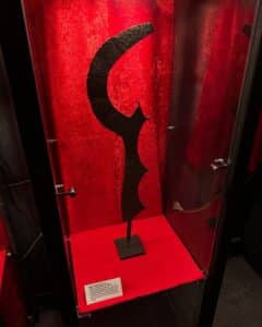 A spiked execution sword encased in glass at the Museum of Torture in Salem, Massachusetts, set against a deep red backdrop with descriptive text in the exhibit.